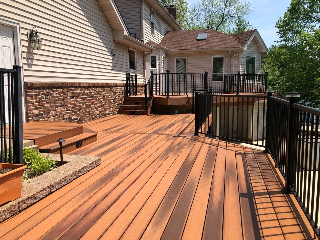 Wooden deck with black railings, connected to a two-story house with a brick and light siding exterior.