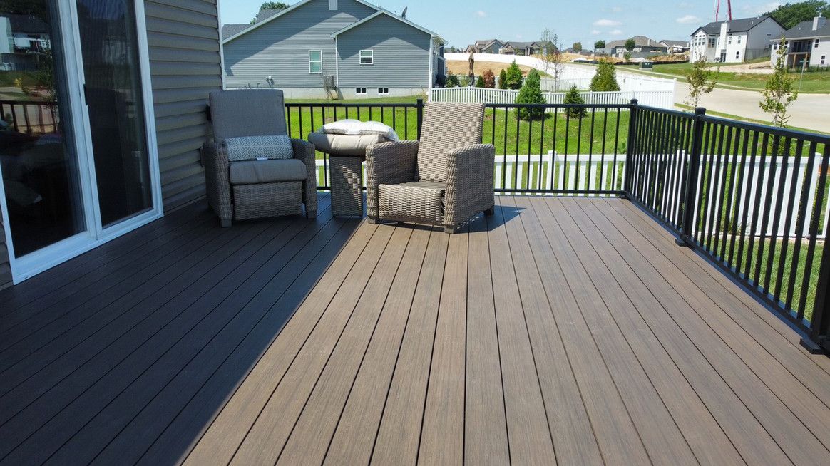 Brown composite deck with outdoor furniture, black railing, and a view of a grassy yard with houses in the background.