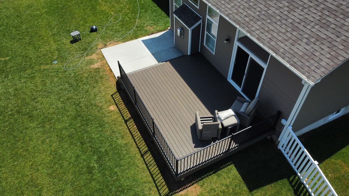 Elevated brown deck with two chairs outside a two-story home, surrounded by green grass.