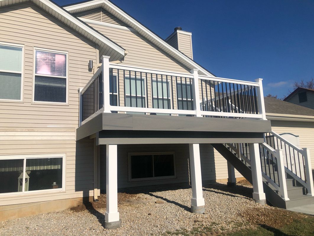A two-story house with a gray deck supported by white columns, under a clear blue sky.