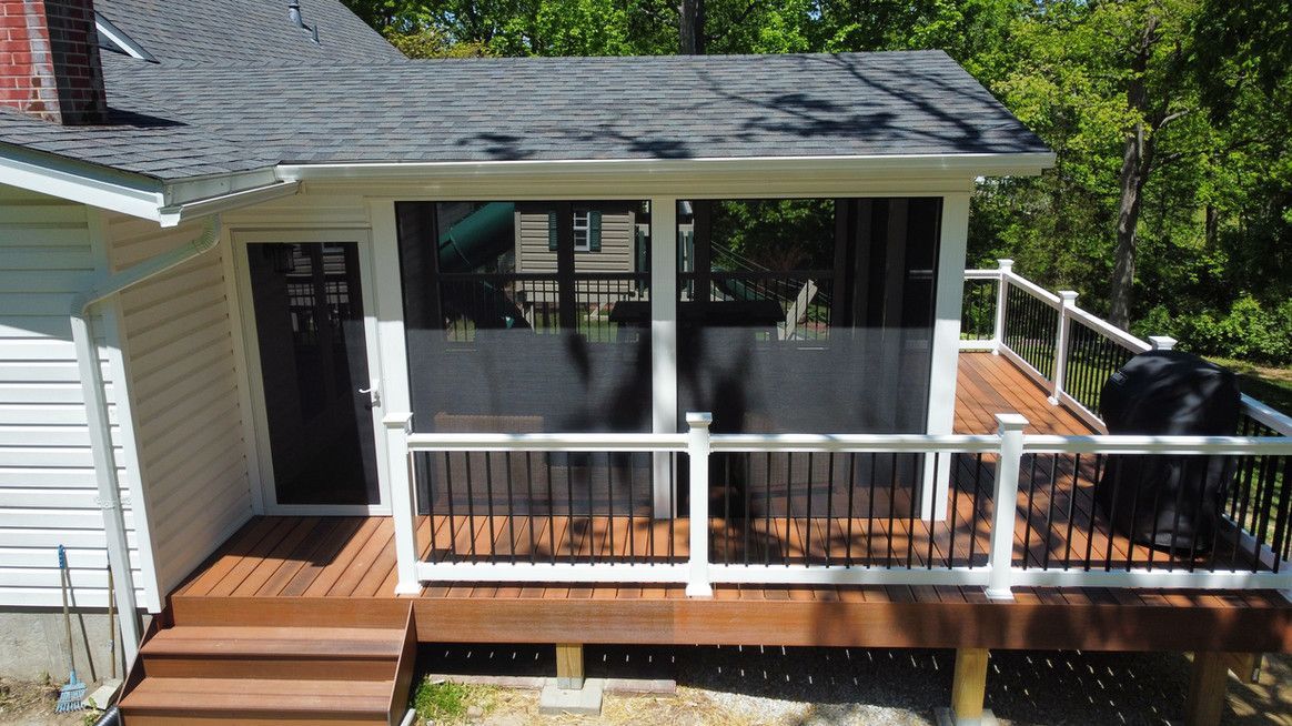 A house with a screened-in porch and wooden deck. The deck has black railings with white posts, and a dark brown door.