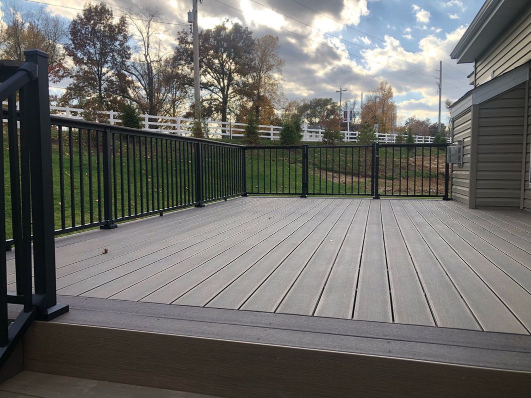 Deck with composite wood flooring and black railing overlooking a yard under a cloudy sky.