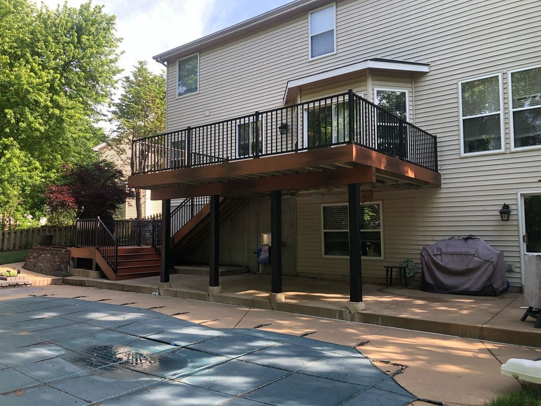 Back of a two-story beige house with a wooden deck over a patio next to a pool.