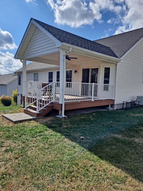 A house with a deck and covered porch on a sunny day. Green grass surrounds it.