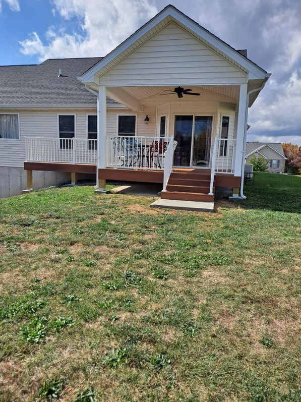 Backyard deck with a covered porch and sliding glass doors. Brown steps, white railings, and tan siding.