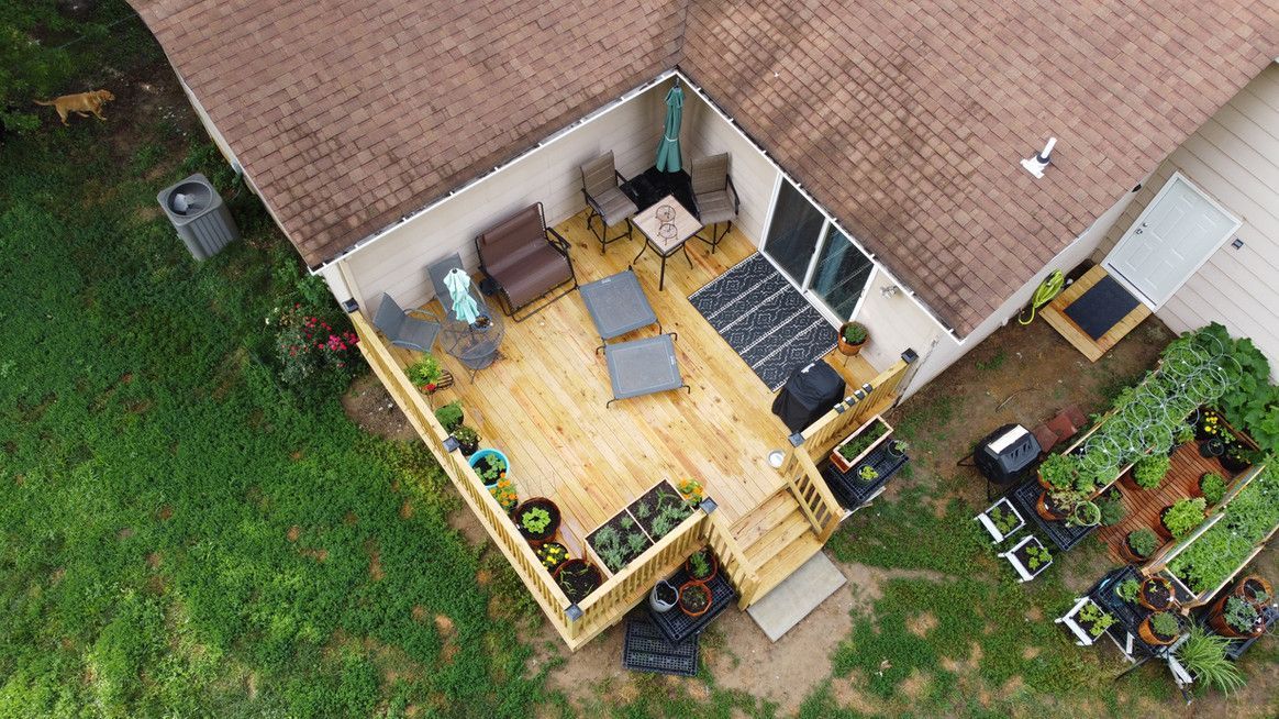 Overhead view of a wooden deck with outdoor furniture, potted plants, and raised garden beds next to a house.
