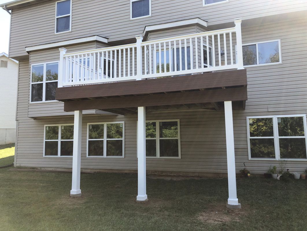 Back of a two-story house with a wooden deck. The deck is elevated and supported by white columns.