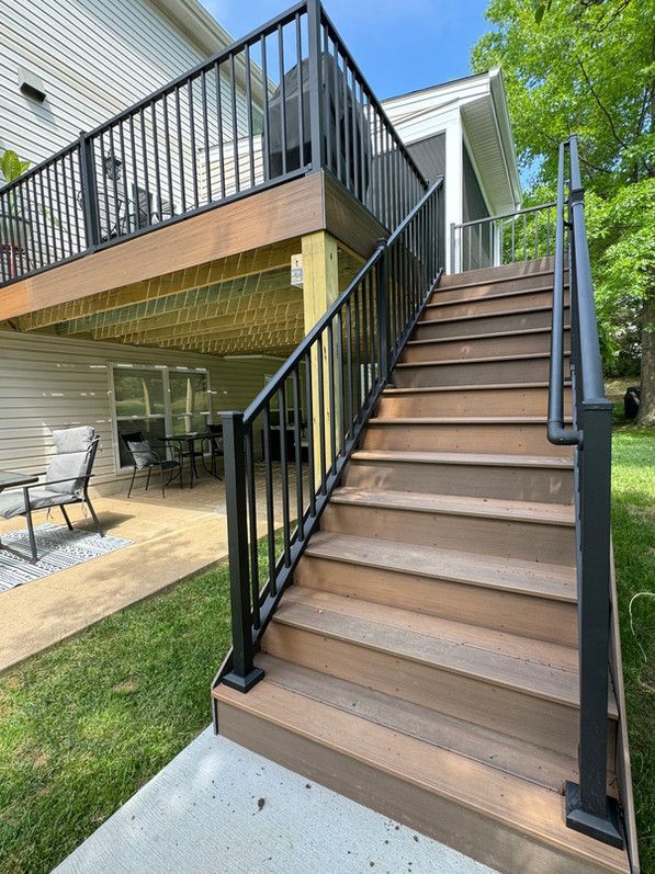 Wooden staircase with black metal railings leading to a deck. Green lawn surrounds the stairs.