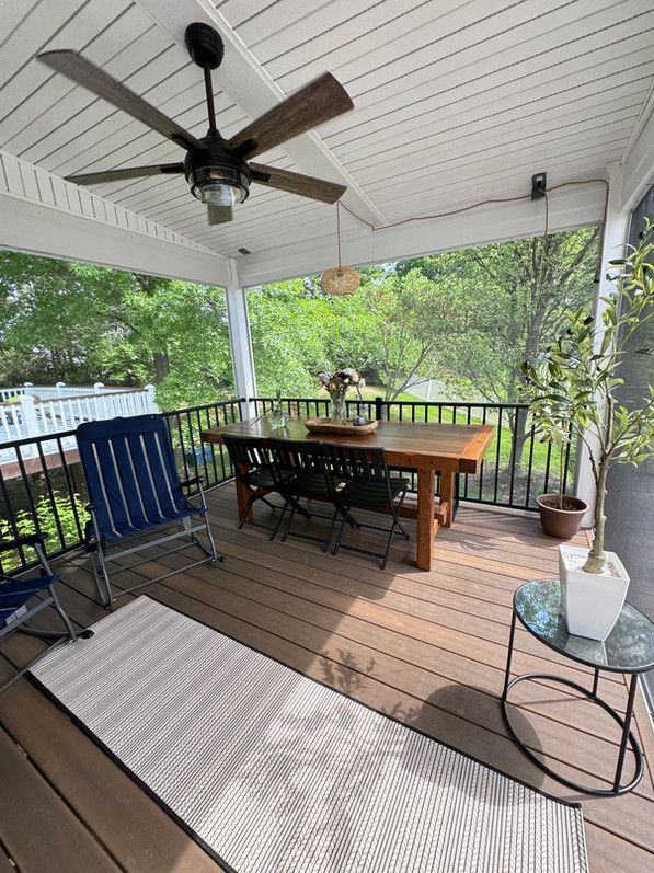Screened-in porch with a wooden table, chairs, fan, rug, and outdoor furniture.