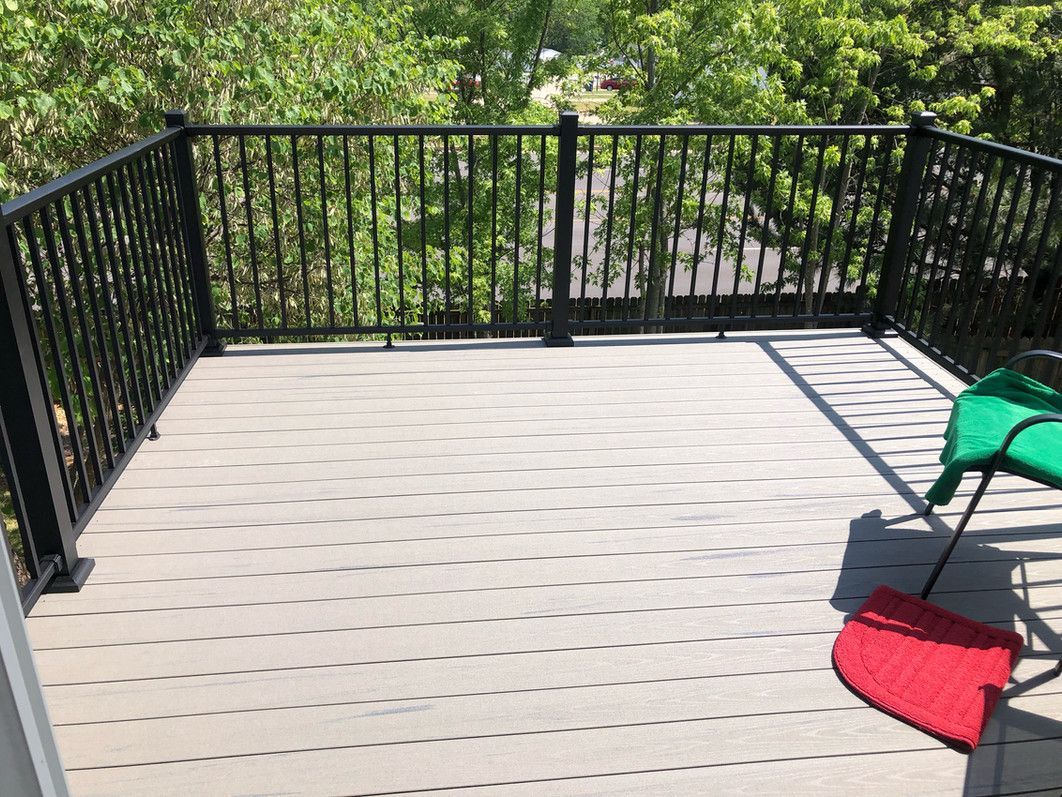 Small deck with black railing and gray decking, green chair and red mat.