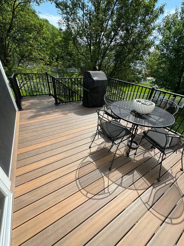 Deck with black grill, table, chairs, and black railing. Trees in background.