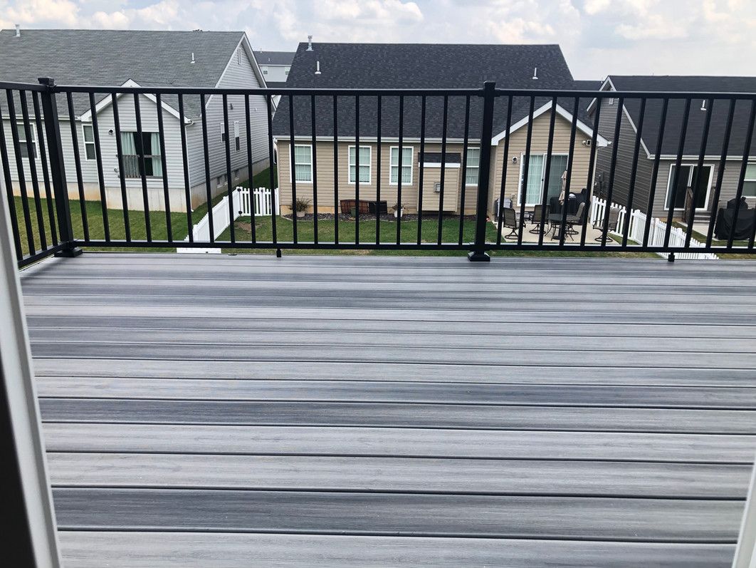 Wooden deck with black railing overlooking several houses.