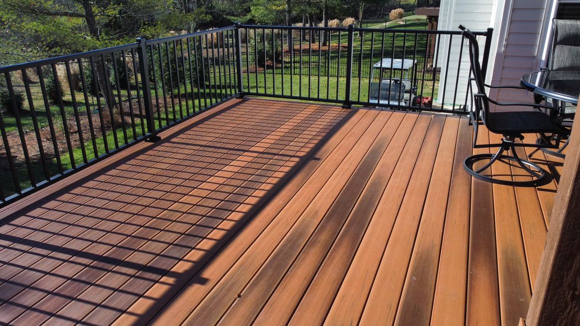 Brown wooden deck with black railings. A shadow from the railing falls on the deck.