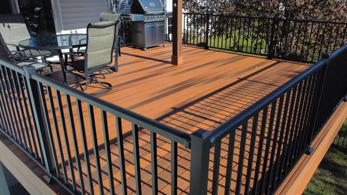 Brown wooden deck with black railings and a grill, patio furniture.