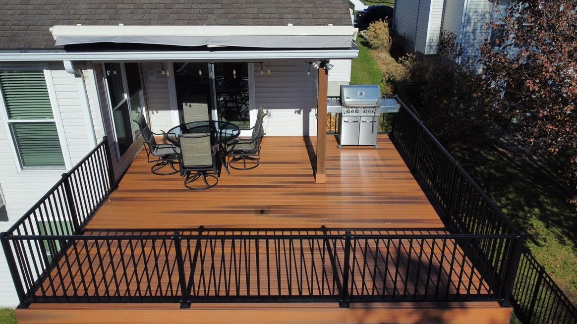 A brown composite deck with black railings and a grill next to a house with sliding doors.