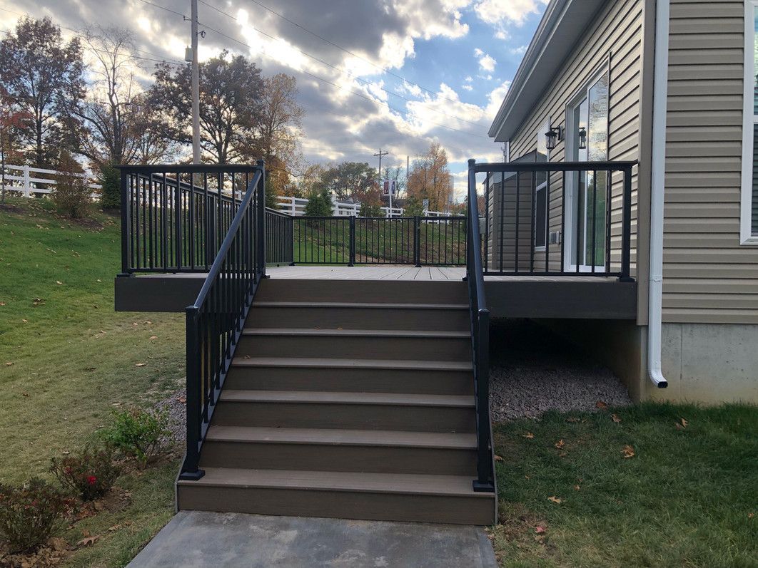 Gray deck stairs with black railings leading to a gray deck next to a house.