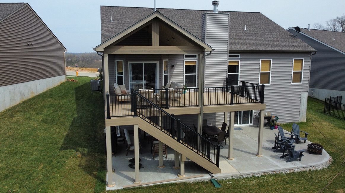 Back of a two-story house with a deck and patio. Brown roof, gray siding, and green grass.