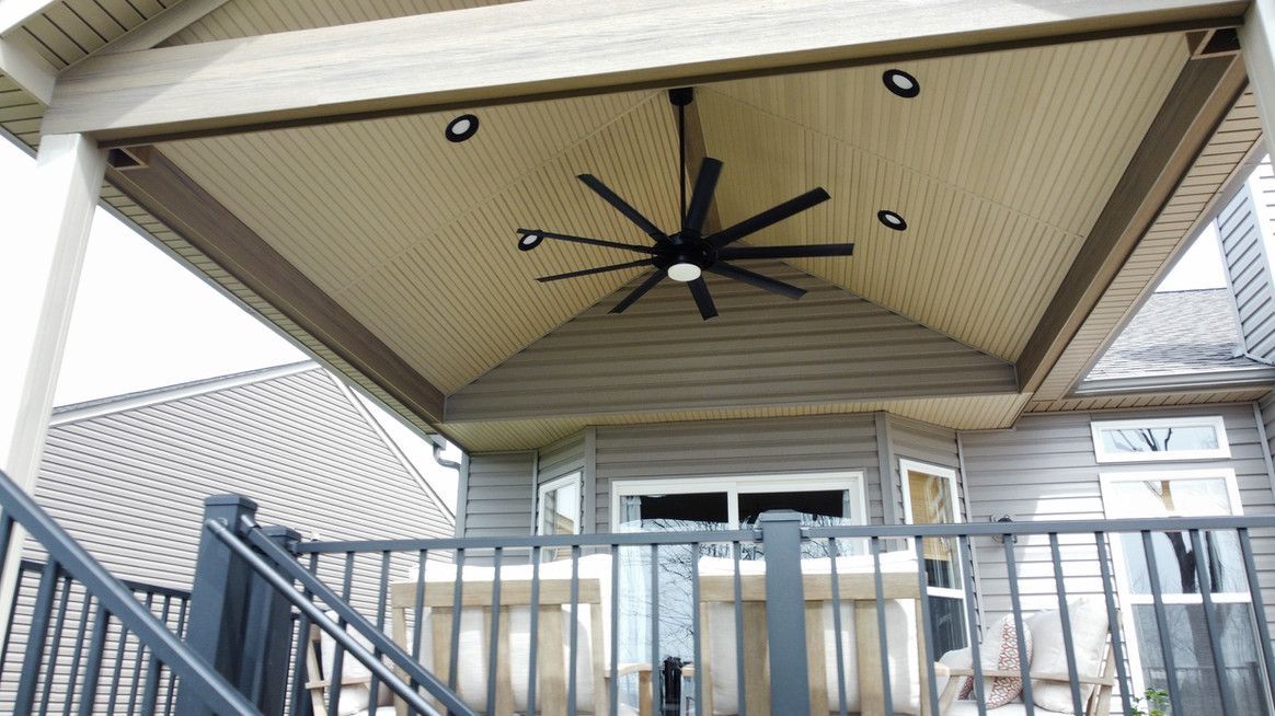 Covered patio with fan and lights over deck with railing and windows.
