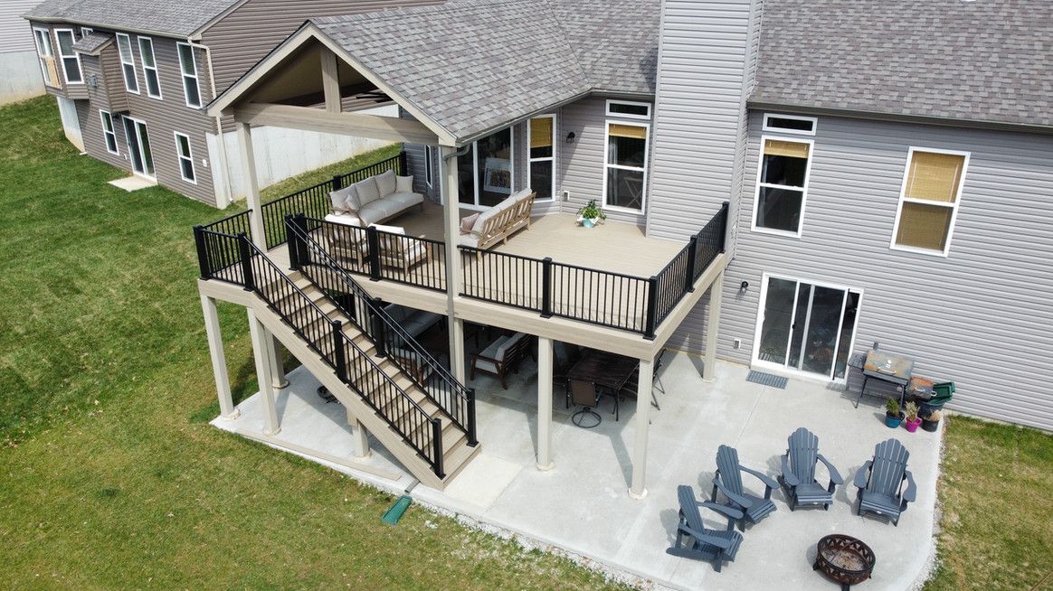 Back of house with deck, stairs, patio, and seating area; gray roof, green lawn.