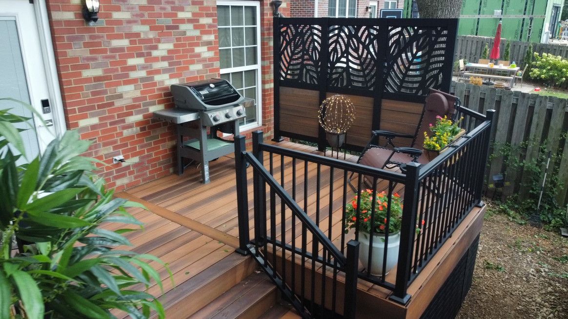 Wooden deck with black railing, grill, privacy screen, and two chairs.