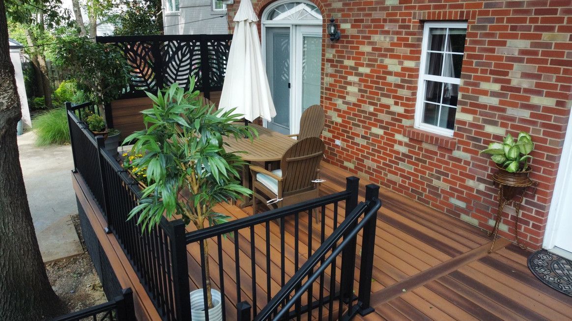 Deck with black railing, table with umbrella, and brick building with a window.