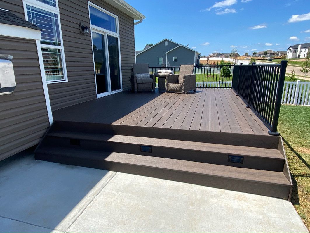 A composite deck with steps, connected to a house with a sliding glass door, and a decorative black railing.
