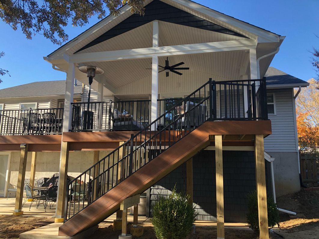 Deck with stairs leading up to covered porch; black railing, brown steps, and a ceiling fan.