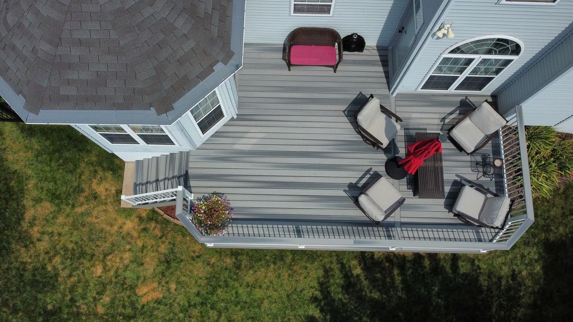 Overhead view of a gray deck with outdoor furniture, beside a house with a gray roof and green grass.