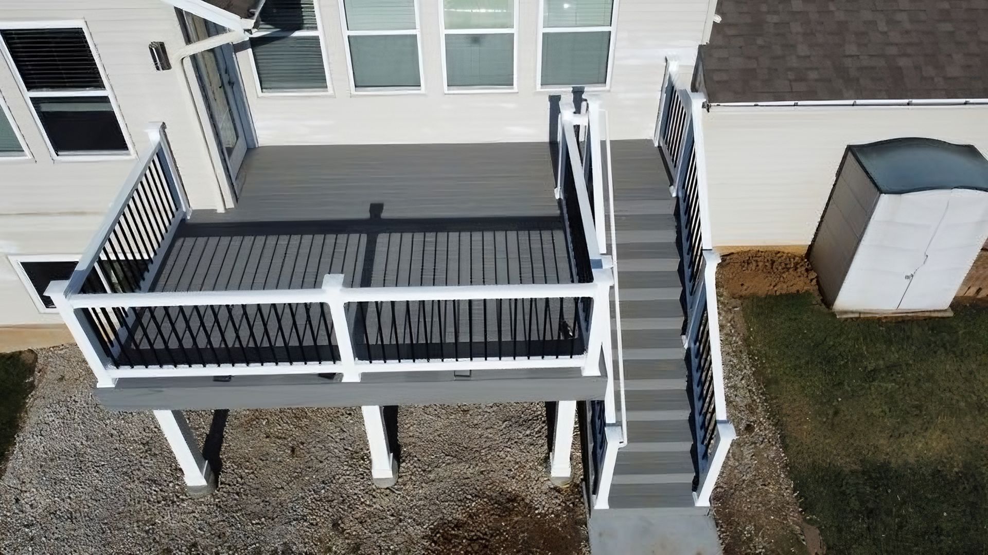 Overhead view of a composite deck with stairs leading to the ground; black railings with white posts and trim.
