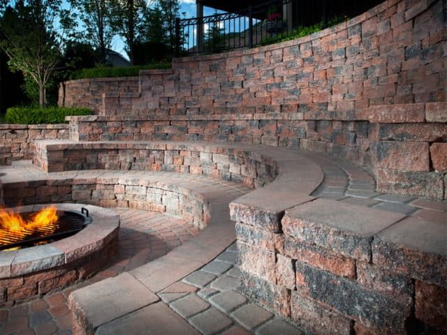 Stone amphitheater retaining wall with curved seating, fire pit, and brick pathways.