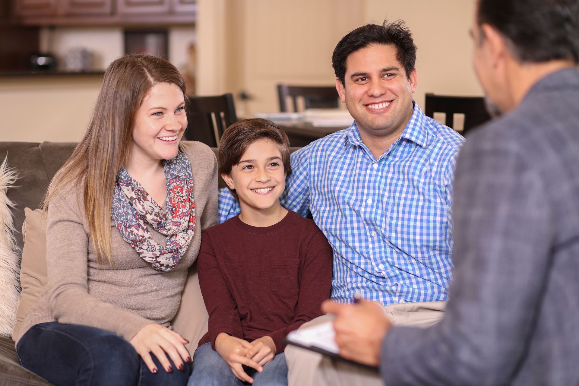 Family Sitting on A Sofa Smiles at A Person Holding a Clipboard in A Living Room — Covington, KY — Mebs Counseling