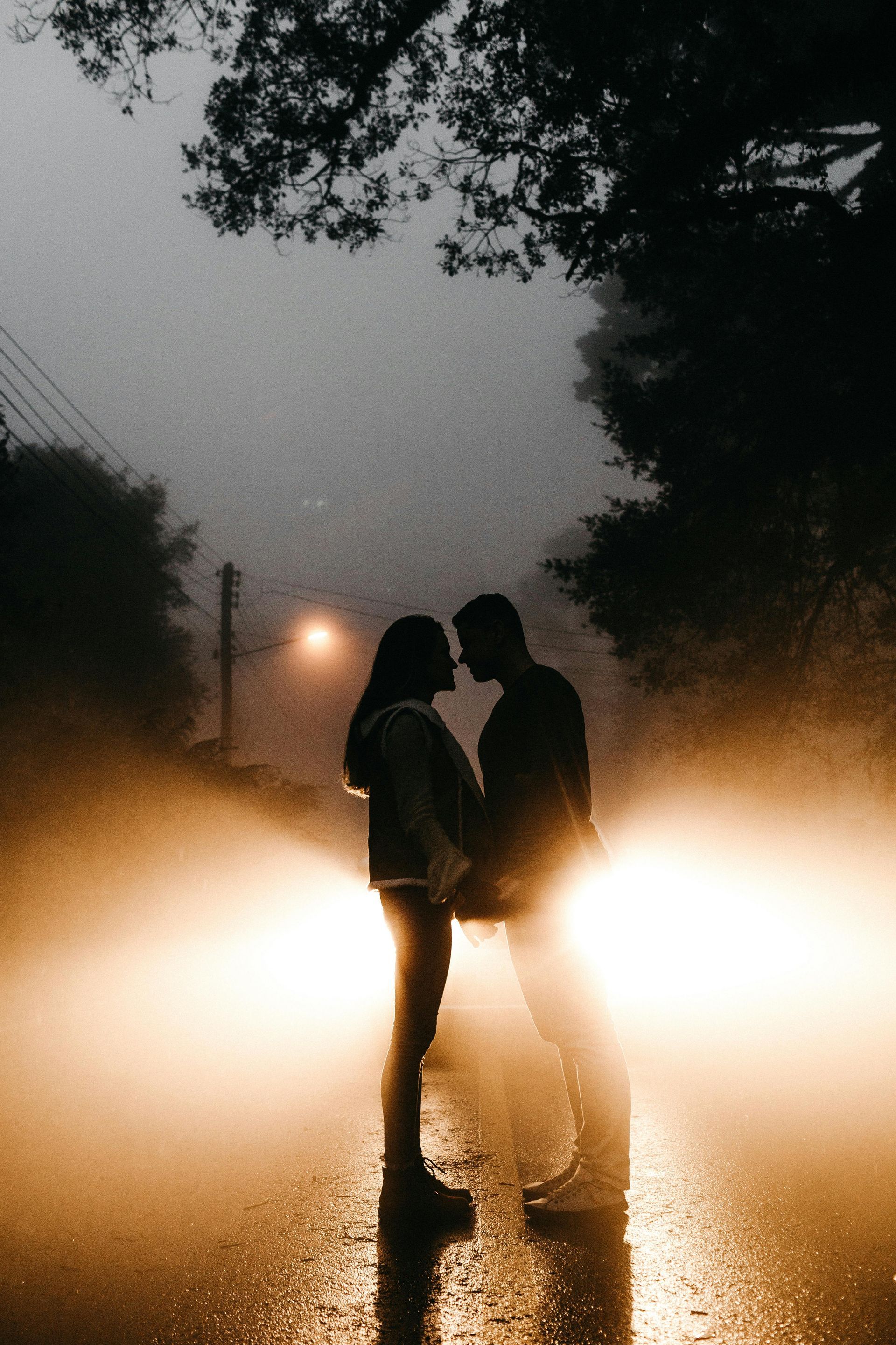 A man and a woman are kissing in front of a car in the rain.