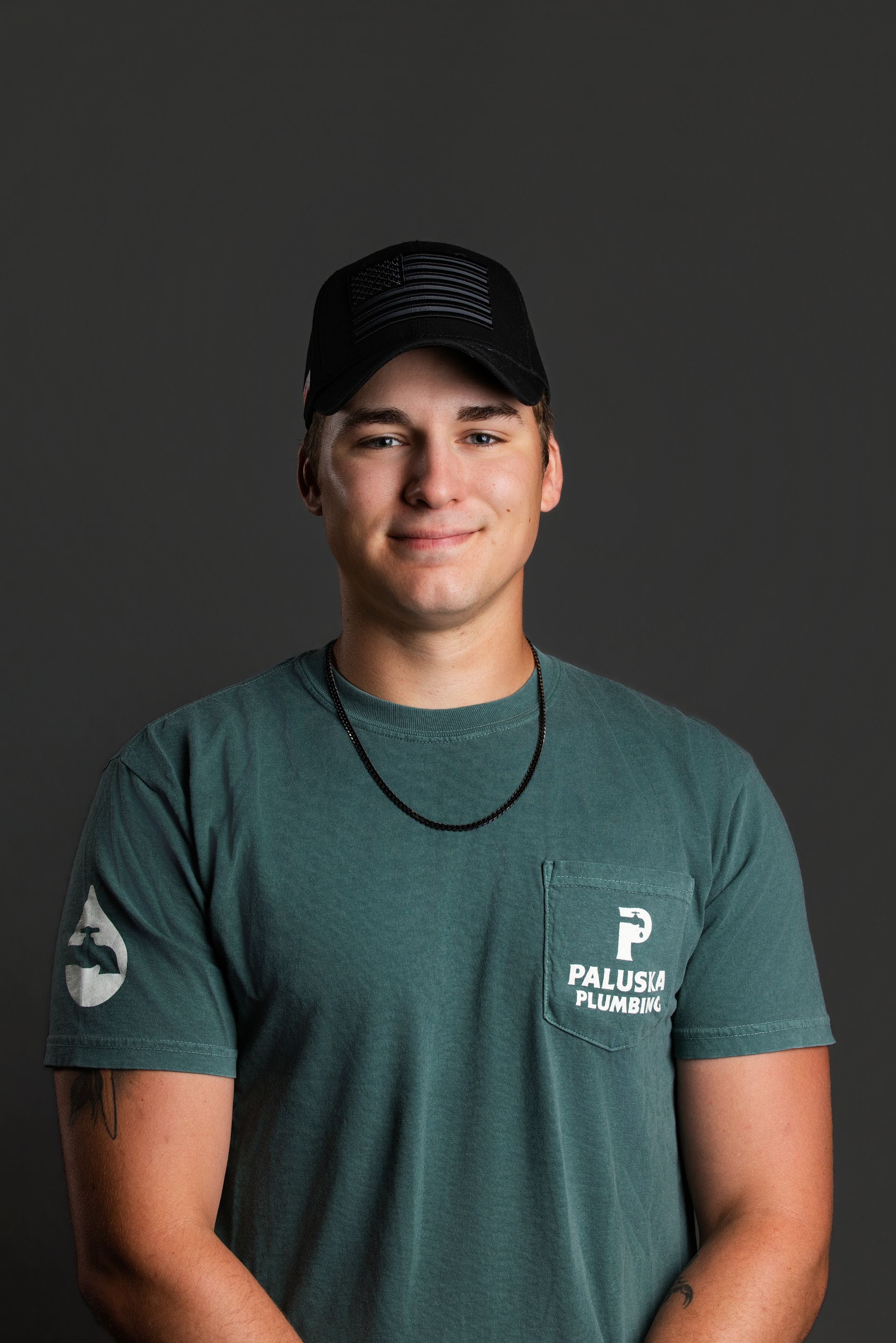 Portrait of a person in a black cap and teal shirt against a dark gray background