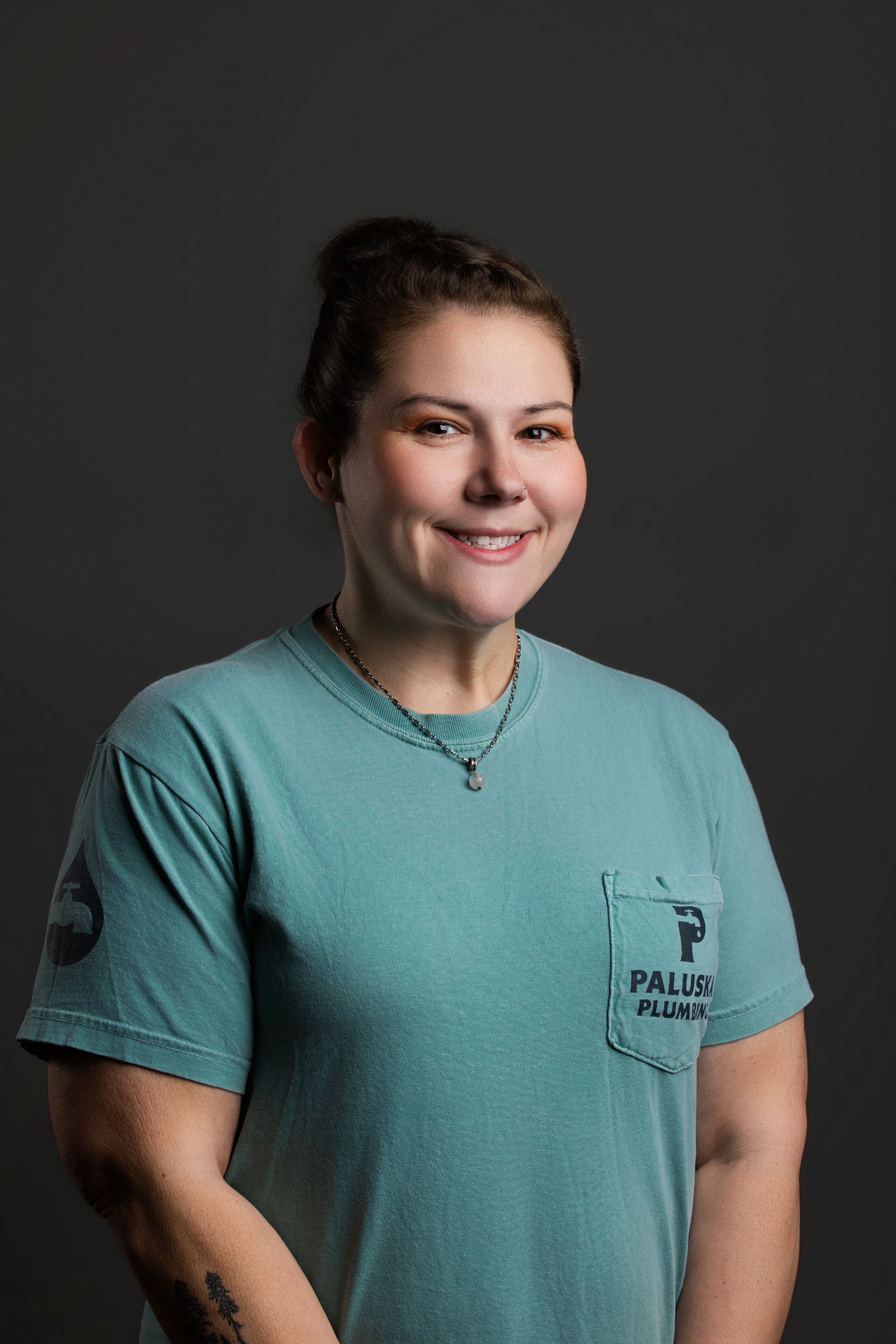 Smiling person in a teal T-shirt standing against a dark gray background