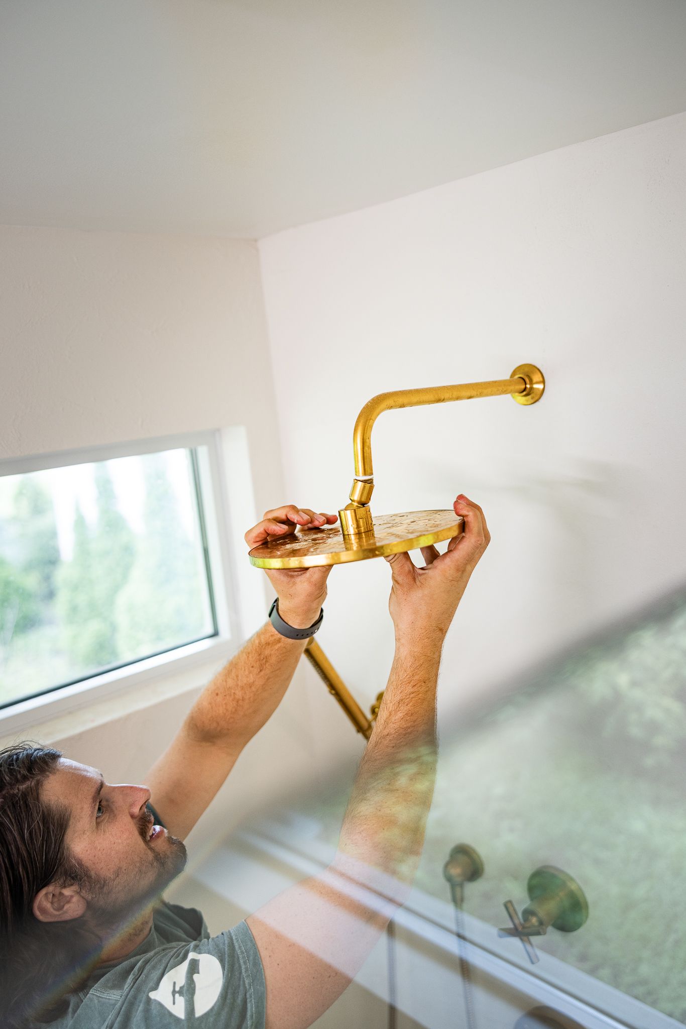 Man installing a gold shower head in a bathroom.