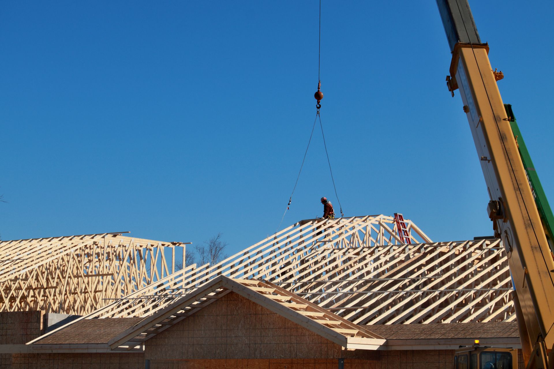 Crane lifting a roof truss at a house construction site.