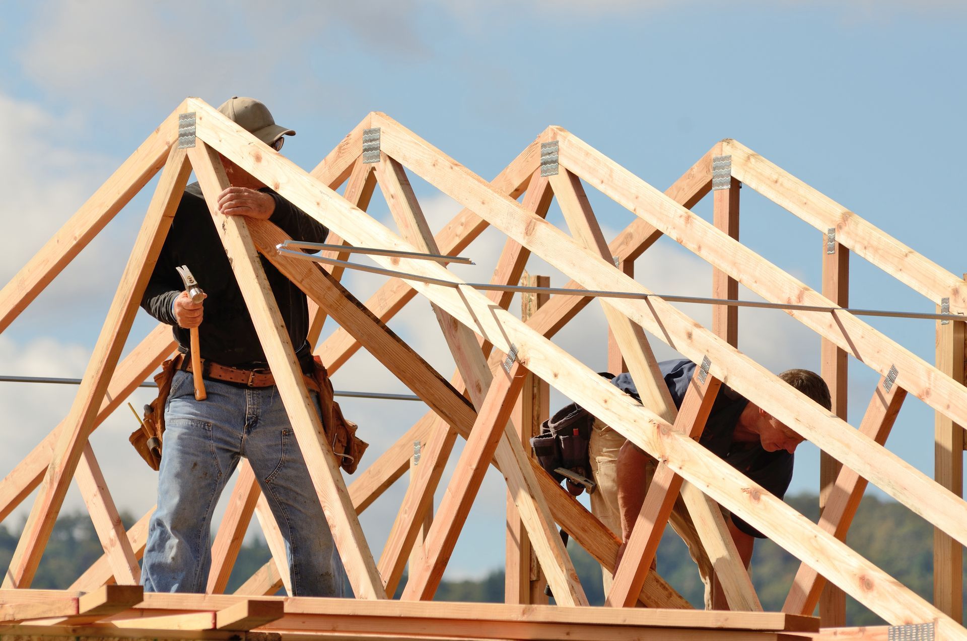 Workers installing engineered wood roof trusses on a building frame.
