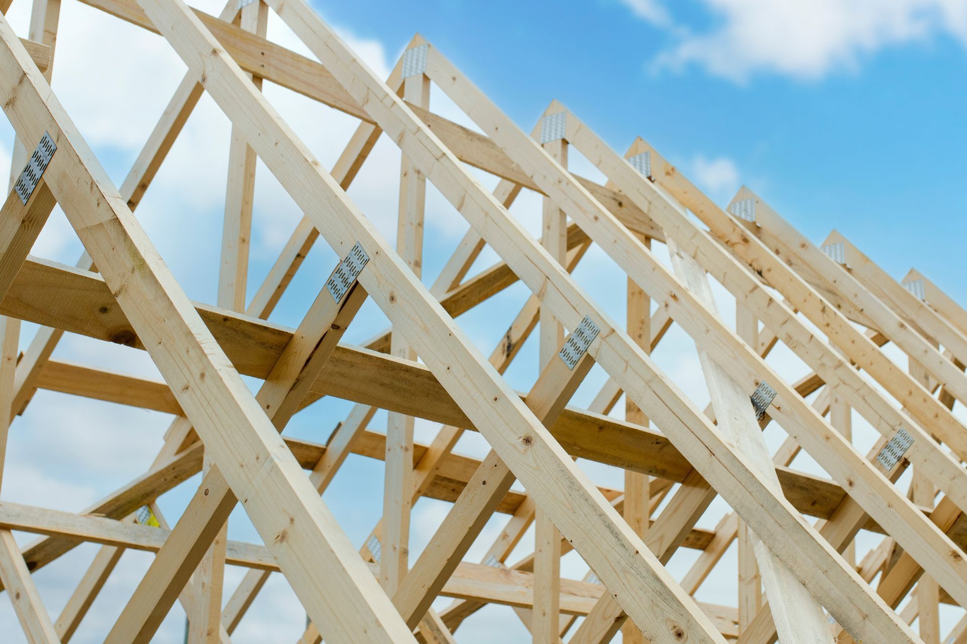 Wooden roof frame under construction against a clear blue sky.