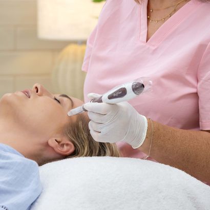 A woman is laying on a bed getting a treatment on her face.