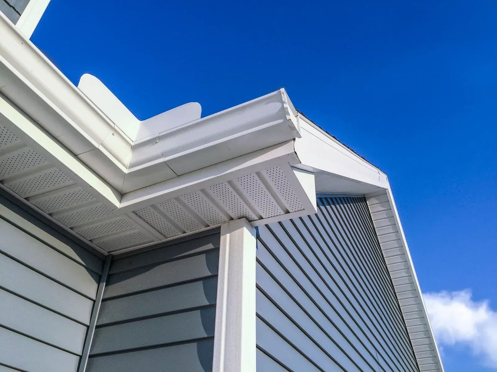 Blue-gray siding with white trim and gutters against a bright blue sky. Corner of a house.