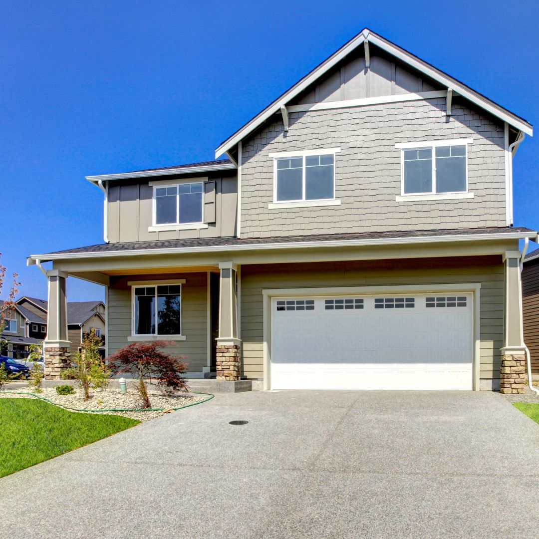 Two-story house with gray siding, white garage door, and a concrete driveway on a sunny day.