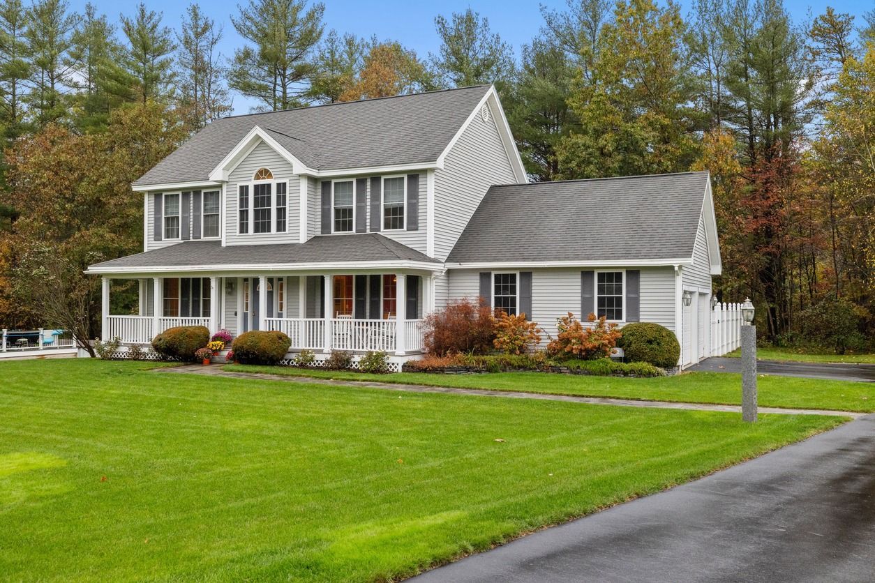 A large white house with a gray roof and a large lawn in front of it.