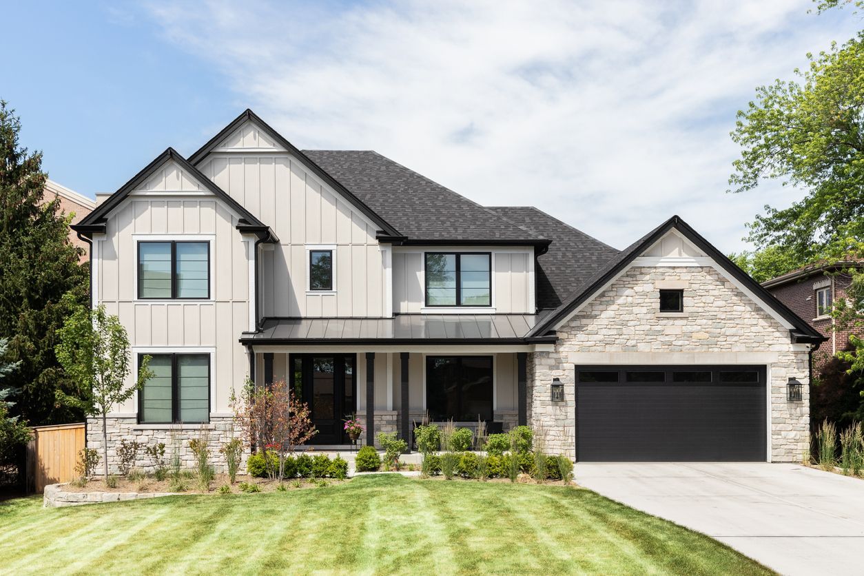 A large white house with a black garage door and a lush green lawn.