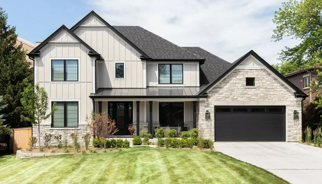 A large house with a black garage door is sitting on top of a lush green lawn.
