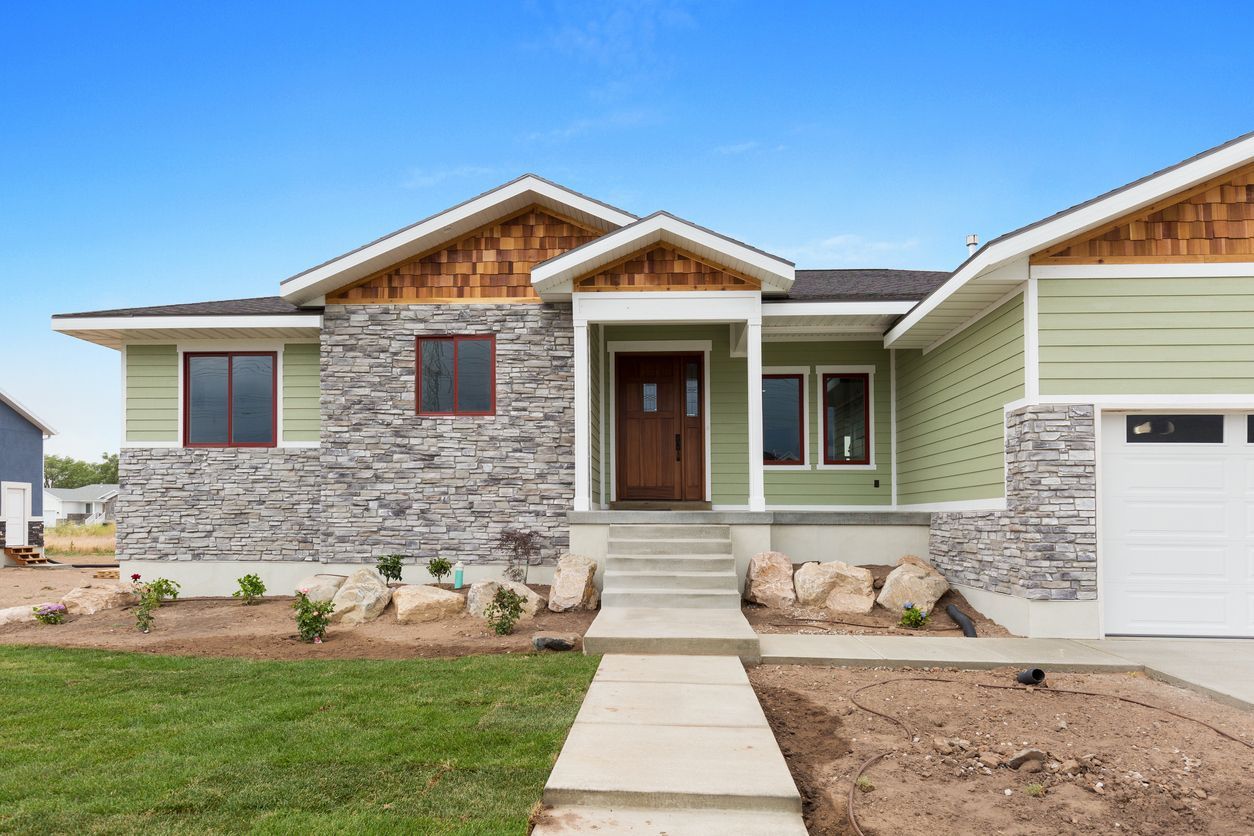 The front of a house with a green siding and a stone facade.