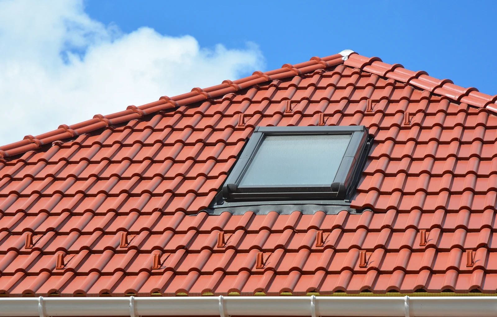 Red tiled roof with a skylight, blue sky background.