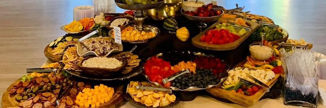 Assorted dishes of food arranged on platters and trays, featuring colorful salads, grains, and desserts.