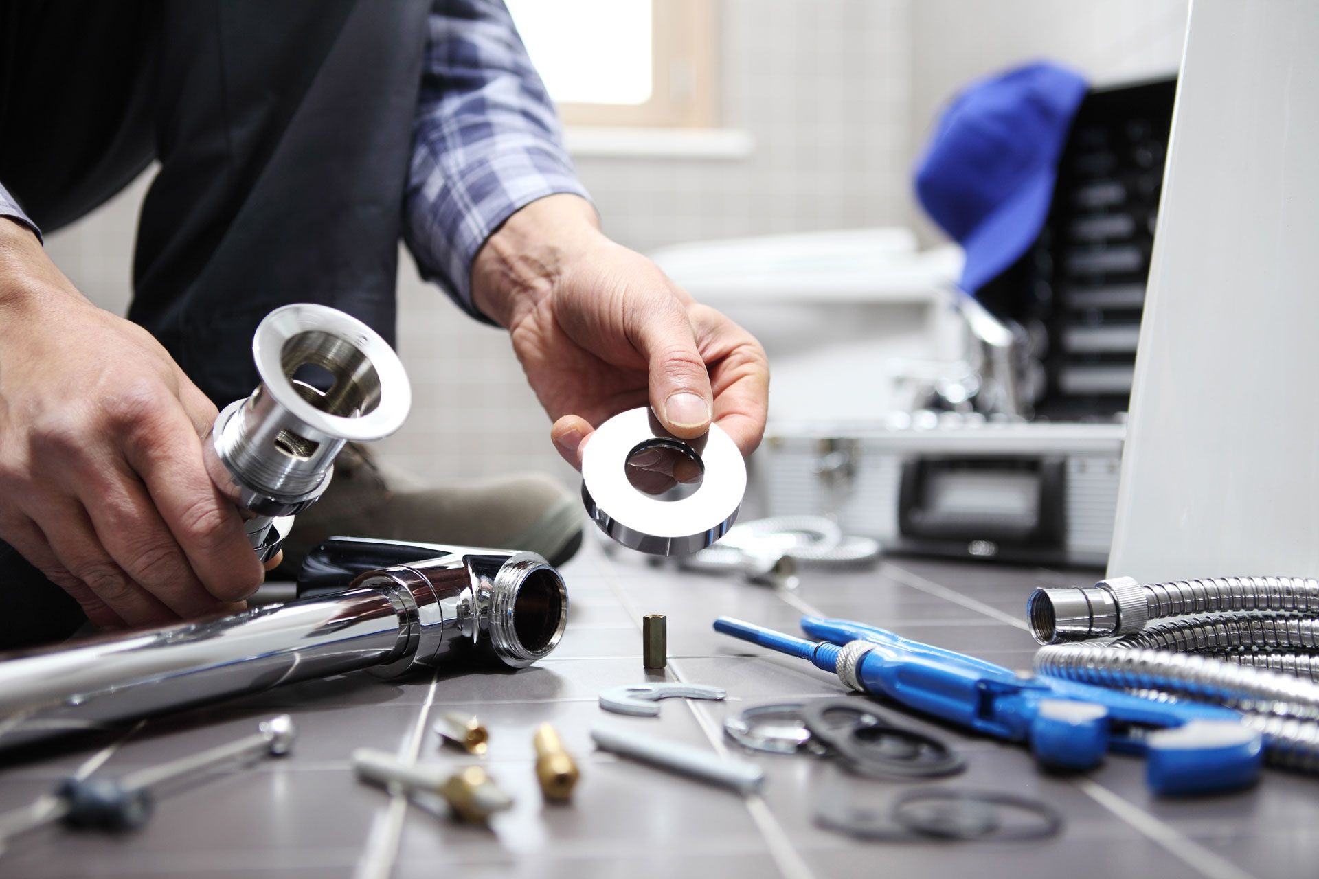 A person assembling chrome plumbing parts on a tiled floor with various tools scattered nearby.