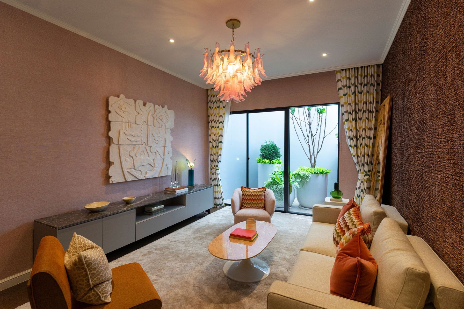 A living room with pink and textured walls, a grey media console, a modern chandelier, a sofa, and patio access.