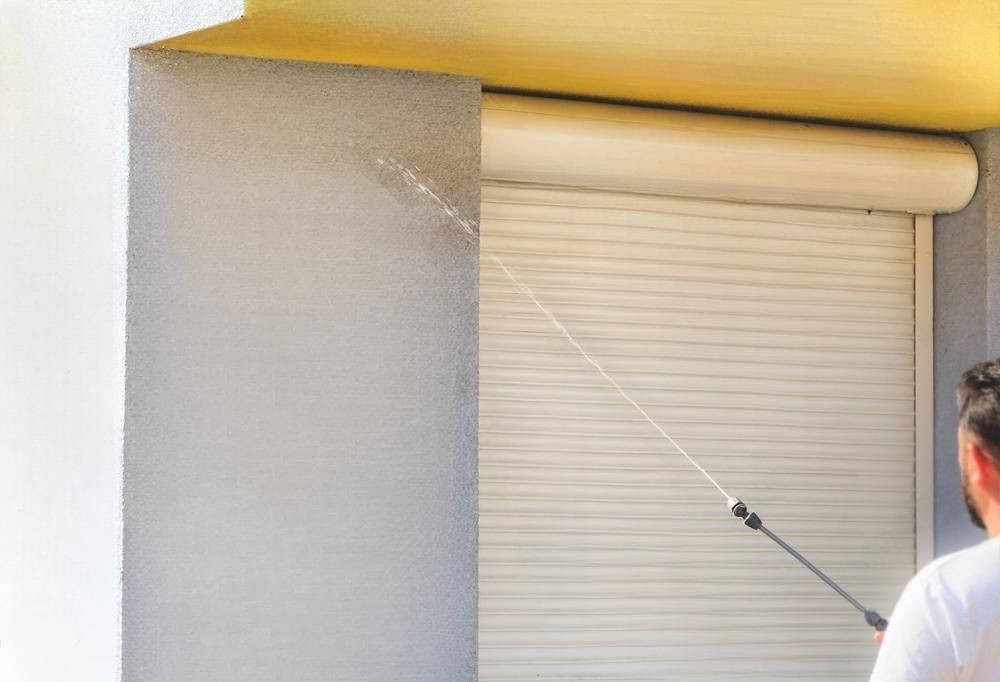 A man is spraying a roller shutter on the side of a building.